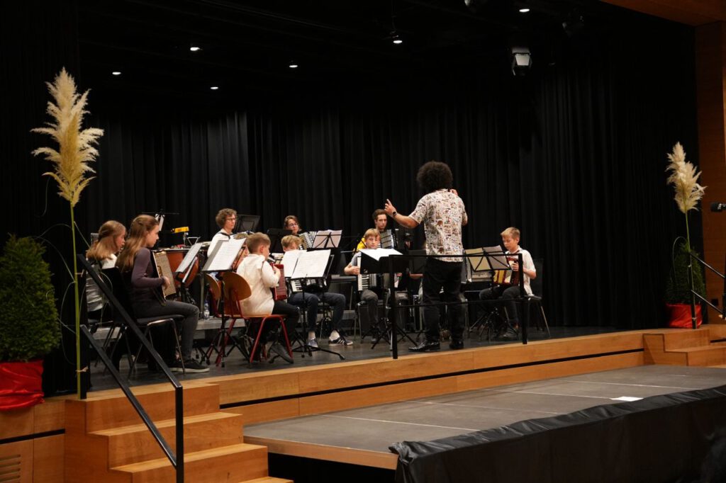 Eine Gruppe von 9 jungen Akkordeon spielenden Personen auf einer Bühne